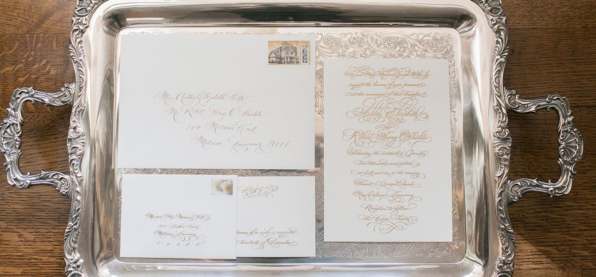 A silver tray filled with wedding invitations and envelopes on a wooden table.