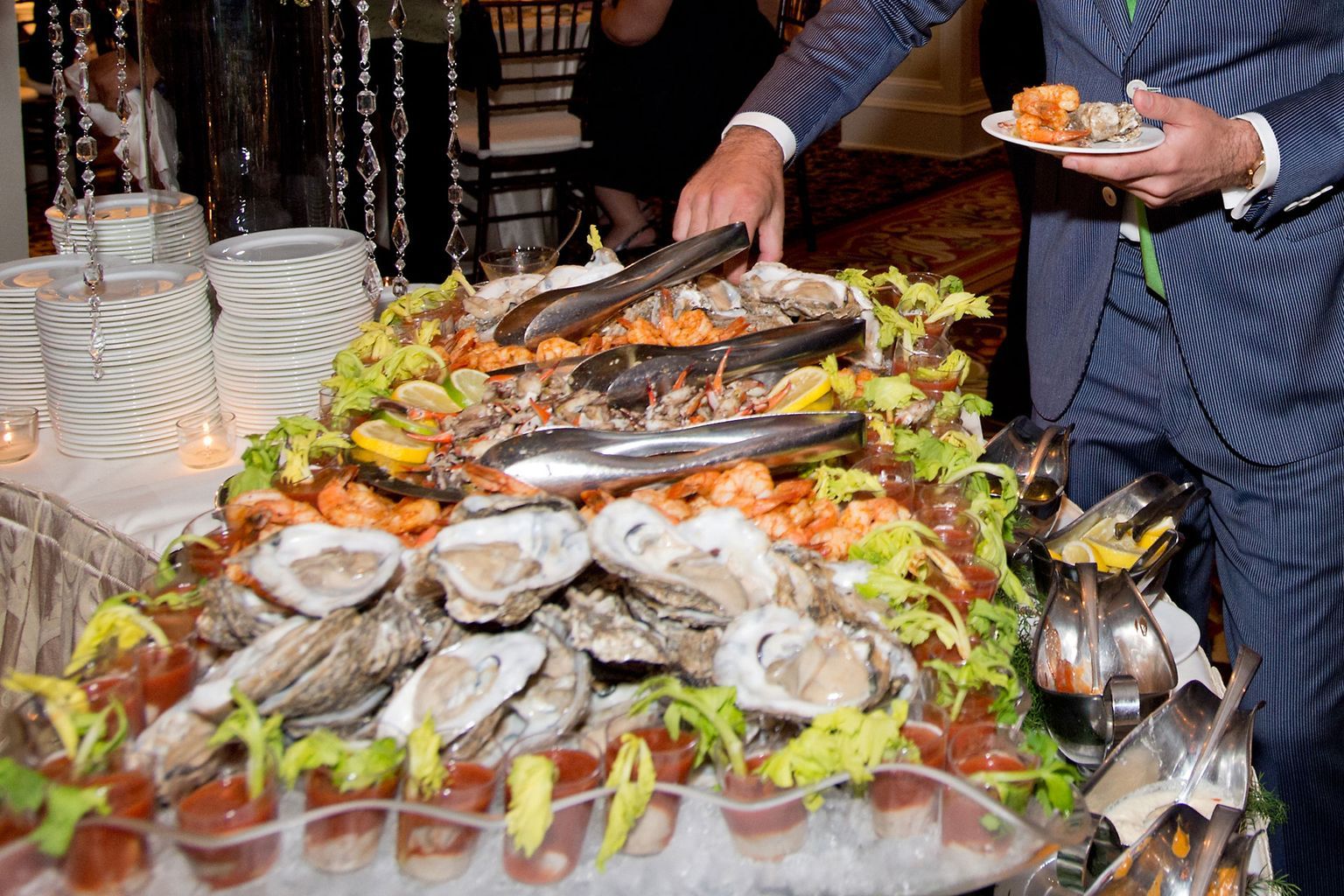 A man is standing in front of a buffet table filled with oysters and shrimp.