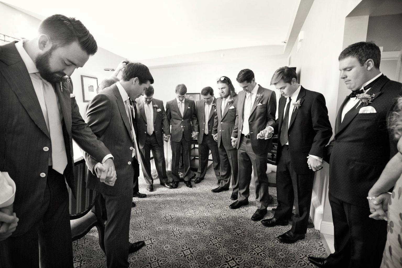 A group of men in suits are praying together in a room.