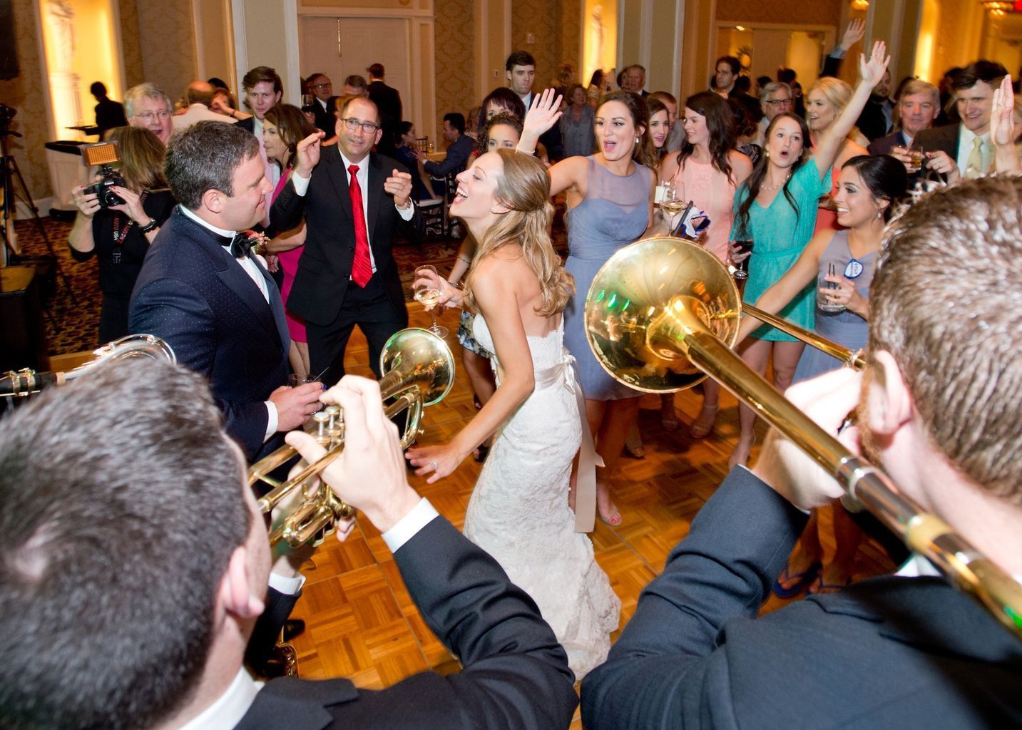 A group of people are dancing at a wedding reception while a man plays a trombone.