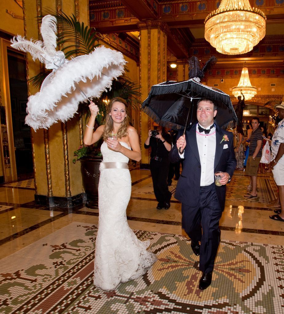 A bride and groom are walking down a hallway holding umbrellas