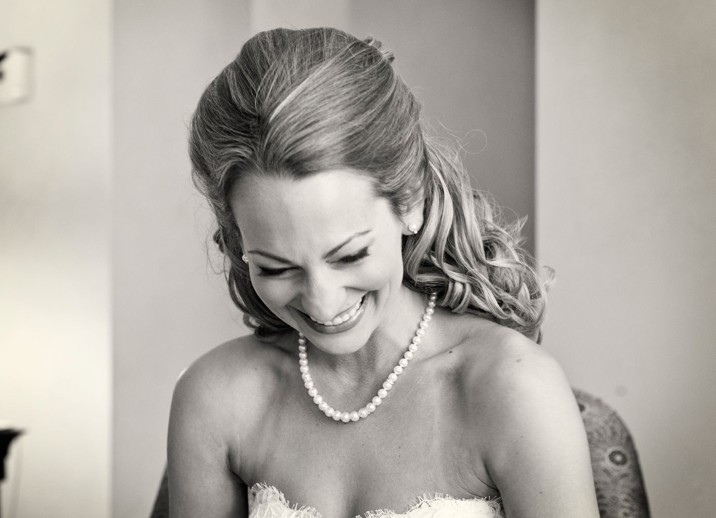 A woman in a wedding dress and pearl necklace is smiling in a black and white photo.