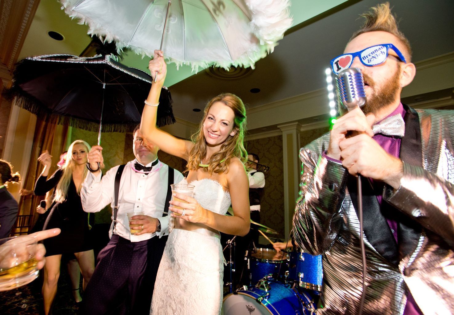 A bride and groom are dancing under umbrellas while a man sings into a microphone.
