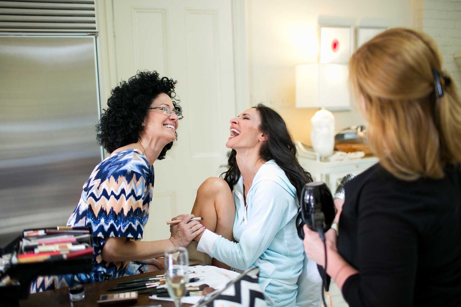 A woman is taking a picture of two women laughing in a kitchen.