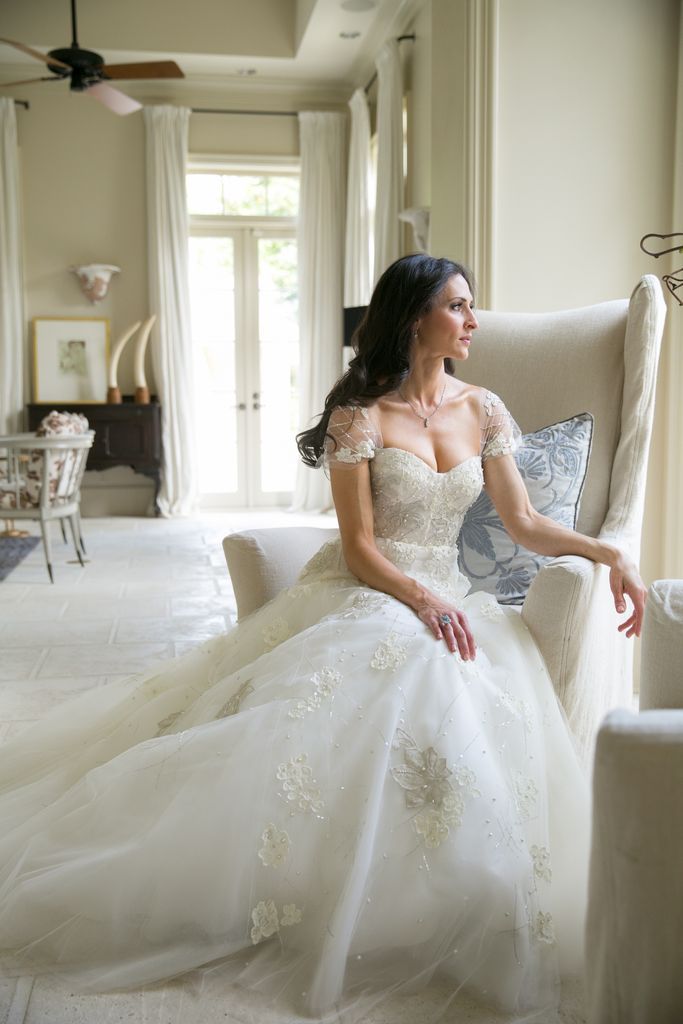 A woman in a wedding dress is sitting in a chair in a living room.