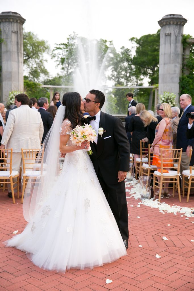 A bride and groom kissing in front of a fountain during their wedding ceremony.