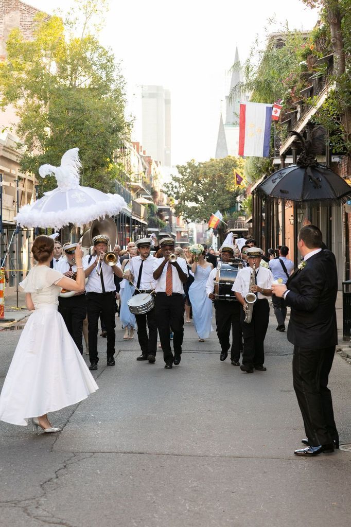 A bride and groom are dancing in front of a marching band.