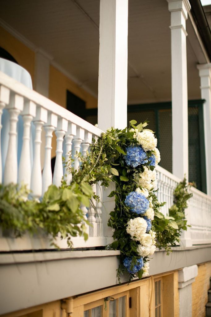 A porch decorated with blue and white flowers and greenery.