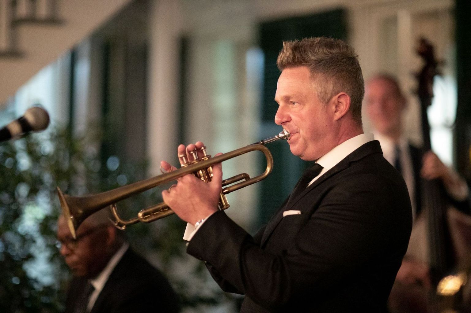 A man in a suit is playing a trumpet in front of a microphone.