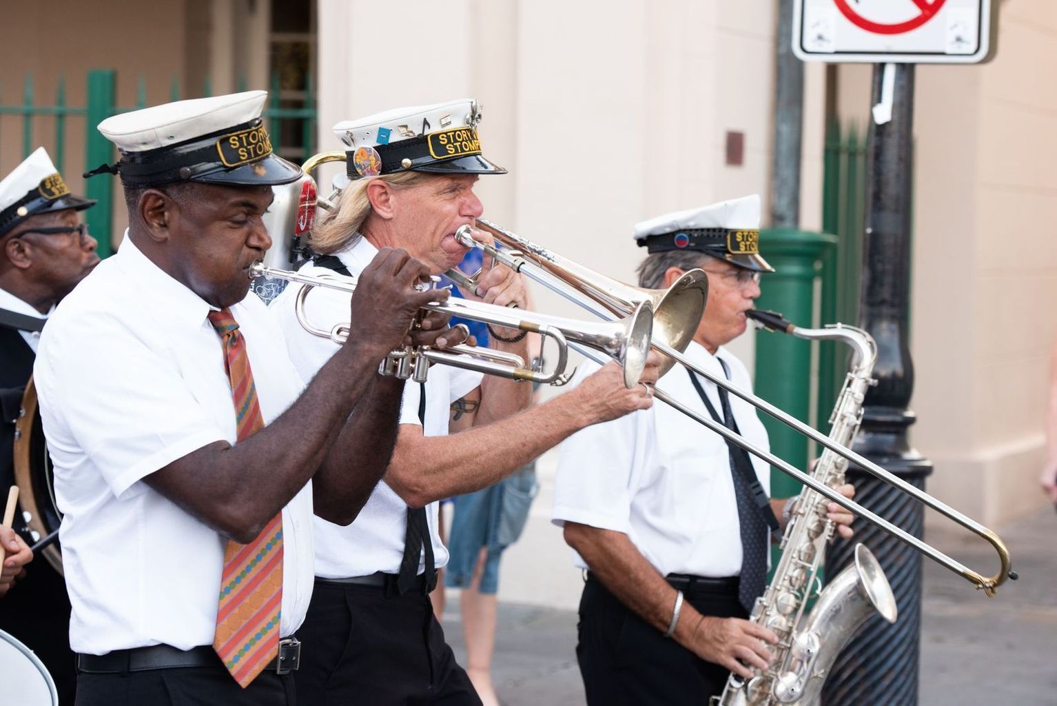 A group of men are playing trombones and saxophones in front of a no parking sign.