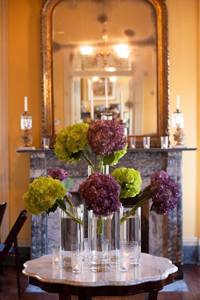 A table with vases of flowers on it in front of a fireplace.