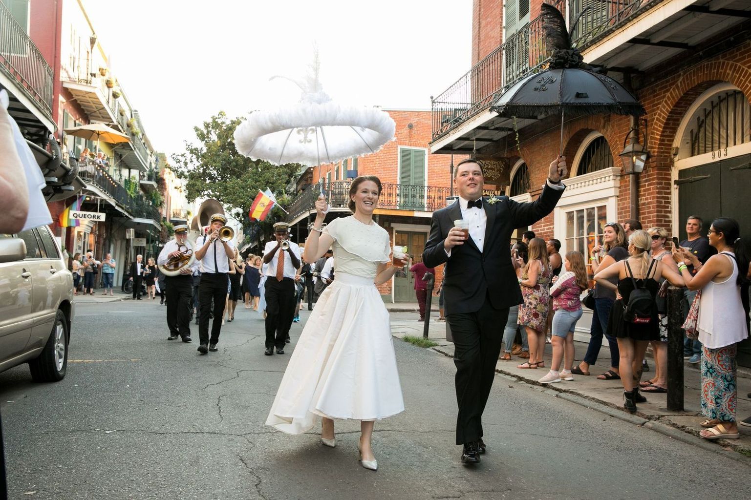 A bride and groom are walking down a street with a band behind them.