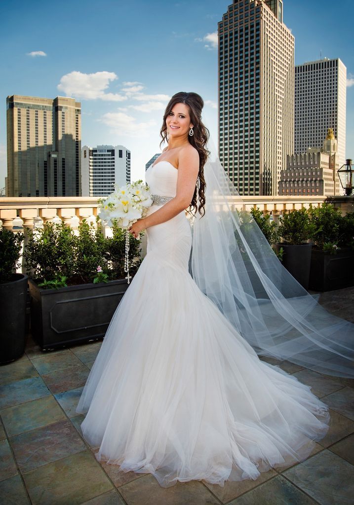 A bride in a wedding dress is standing on a balcony holding a bouquet of flowers.