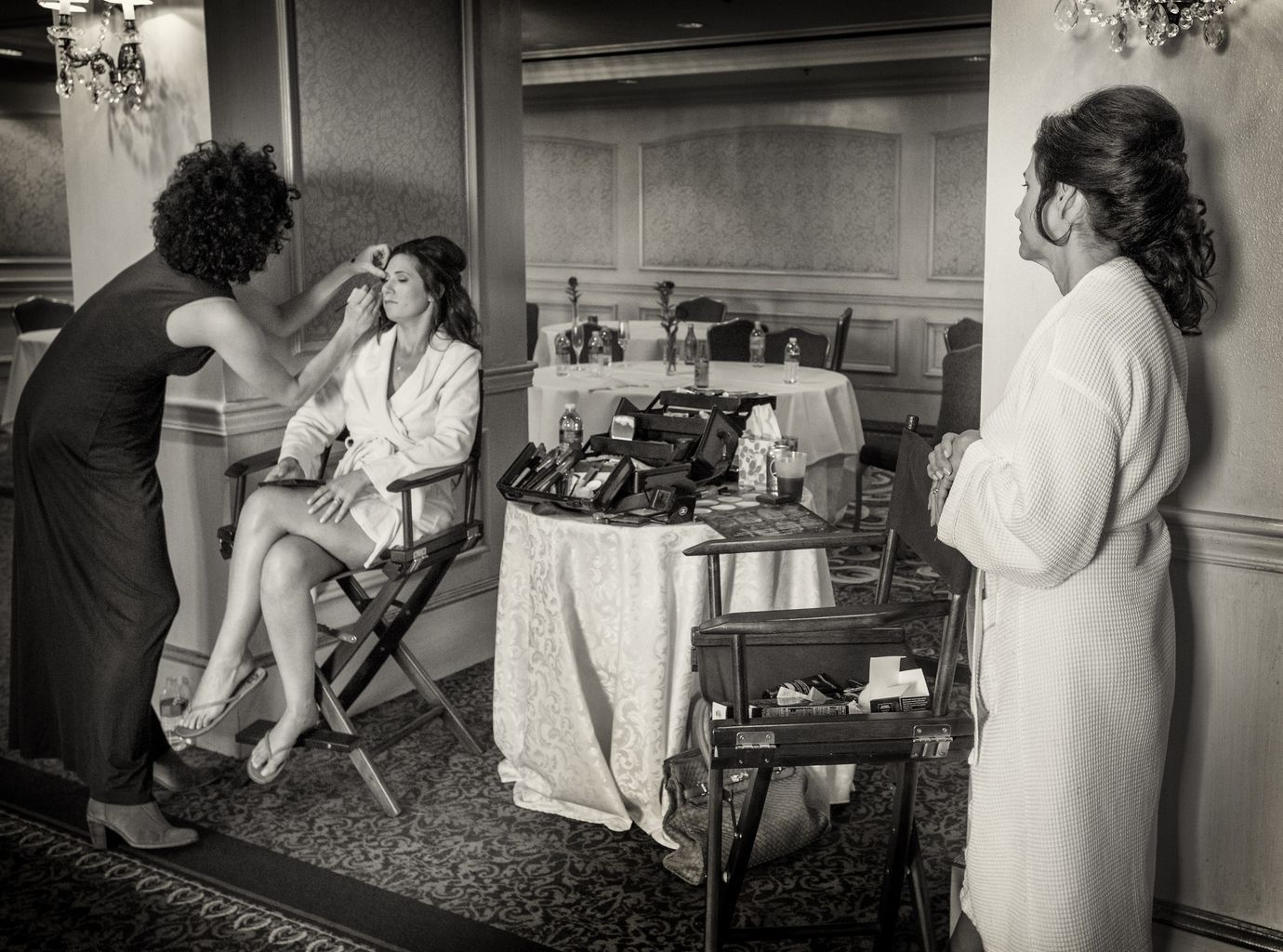 A woman is getting her makeup done in a black and white photo.