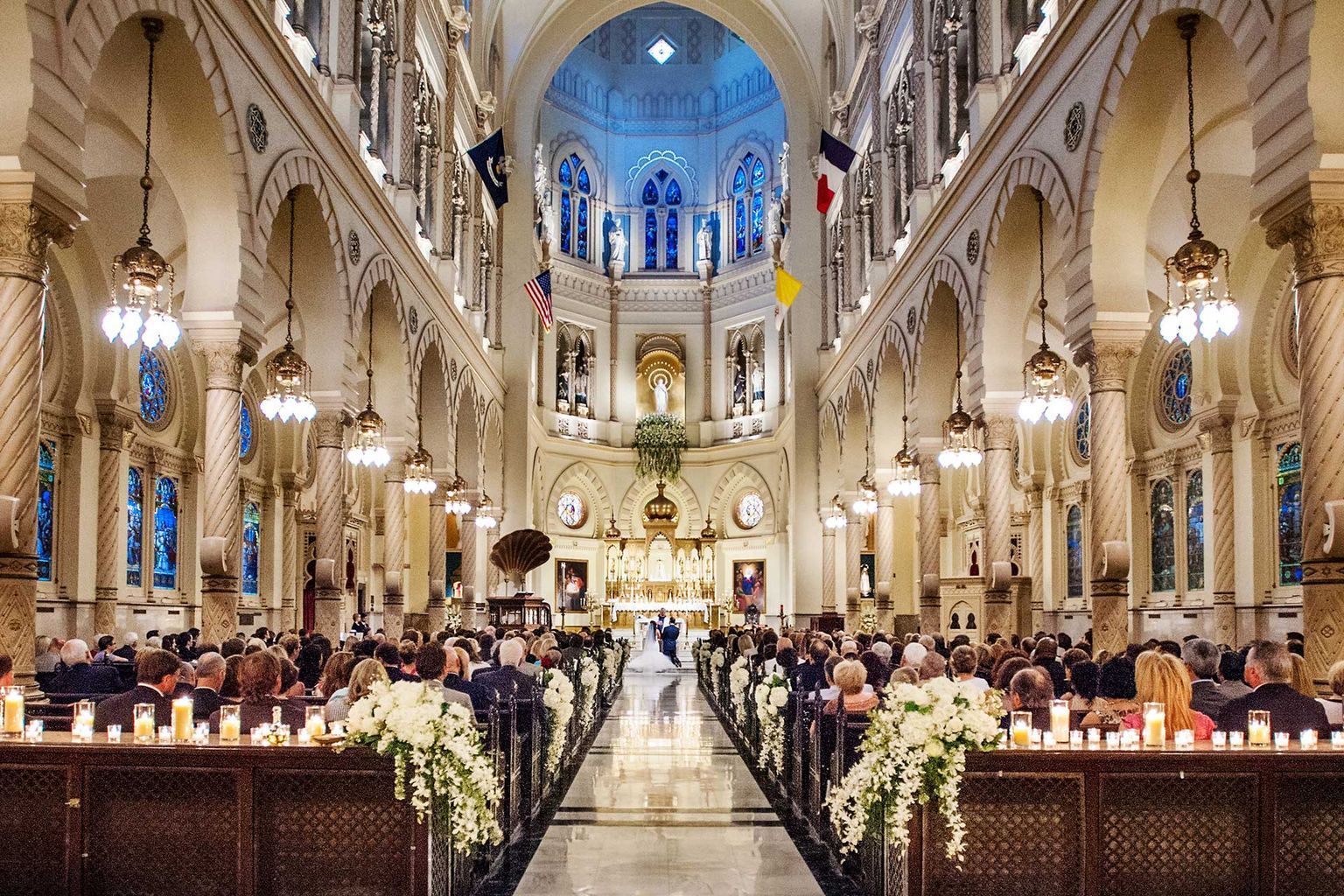 A large church filled with people sitting in the pews and a bride and groom walking down the aisle.
