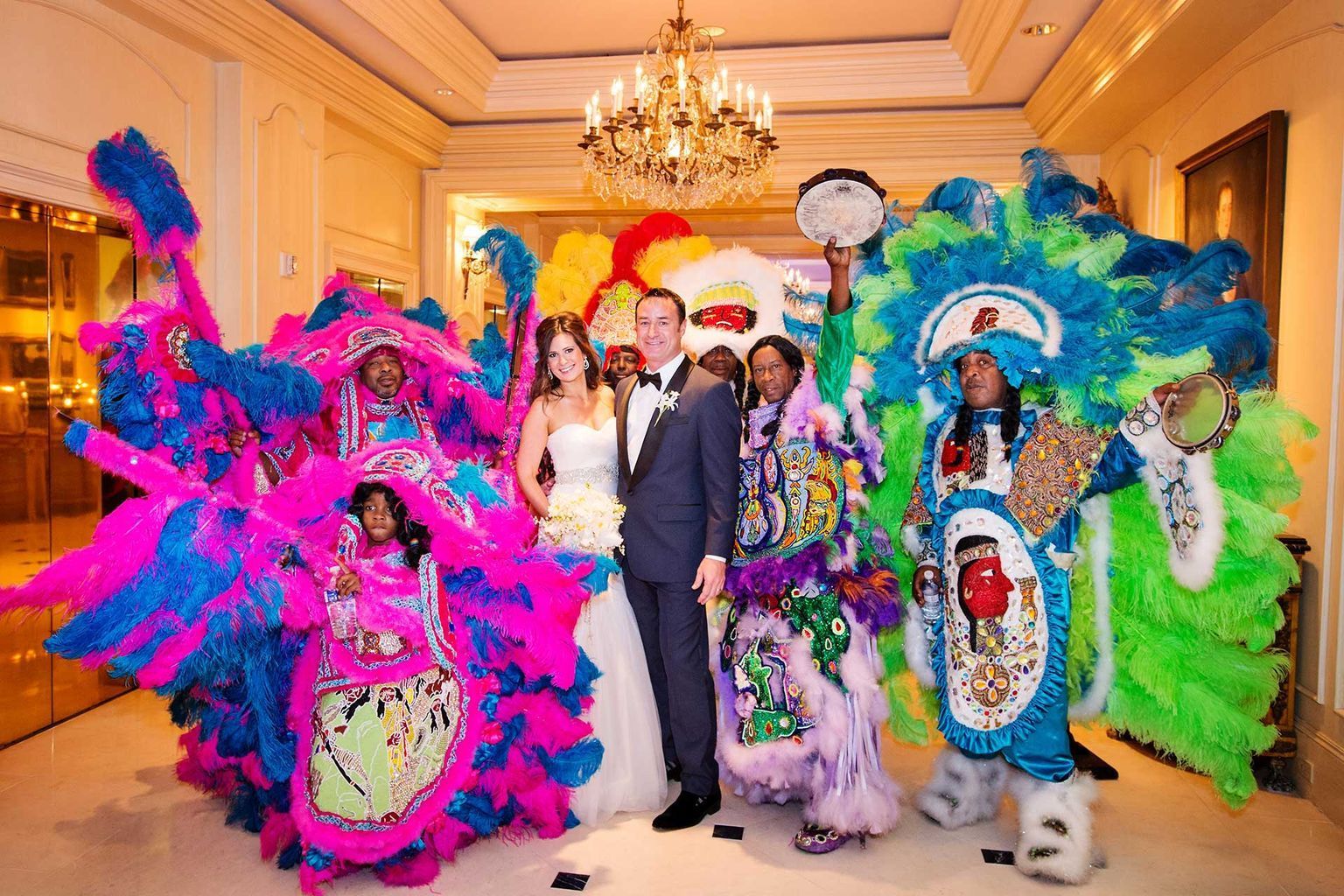 A bride and groom are posing for a picture with a group of people in colorful costumes.