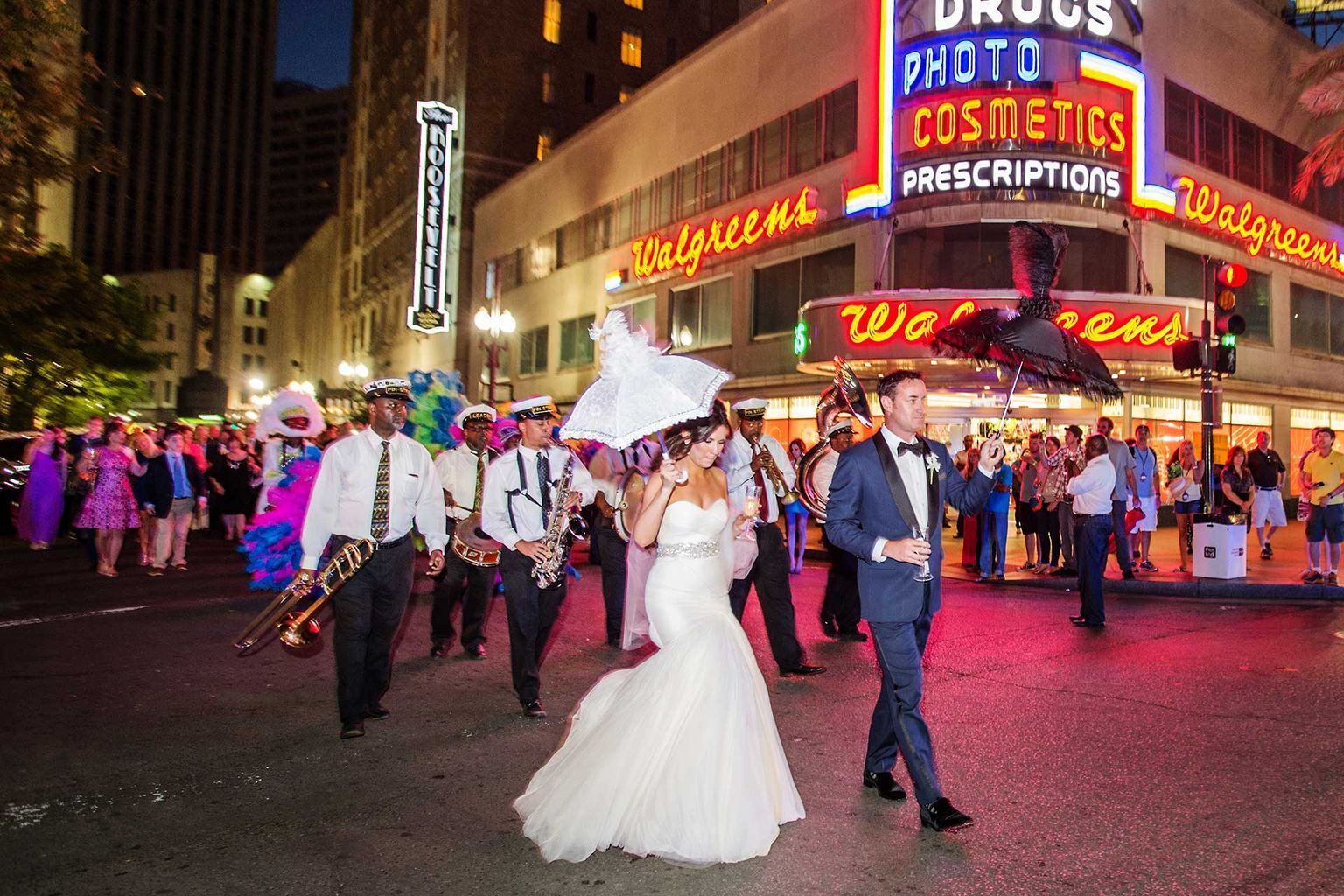 A bride and groom are walking down the street with a band.