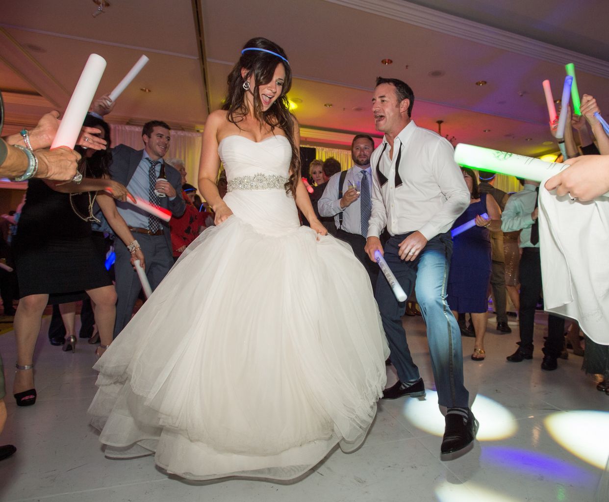 A bride and groom are dancing with glow in the dark sticks