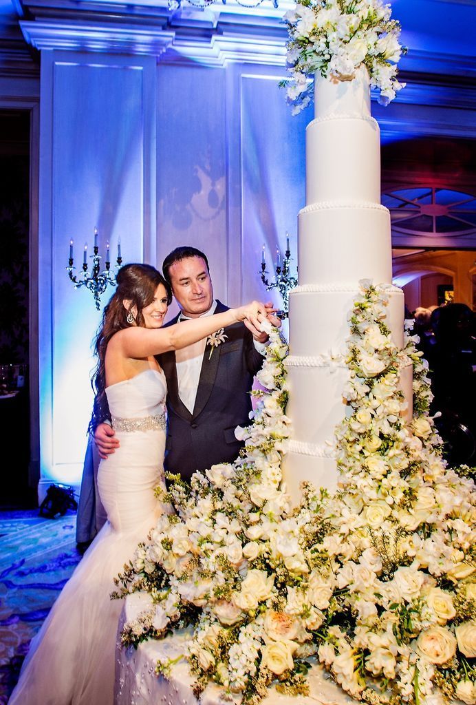 A bride and groom are cutting a very tall wedding cake.