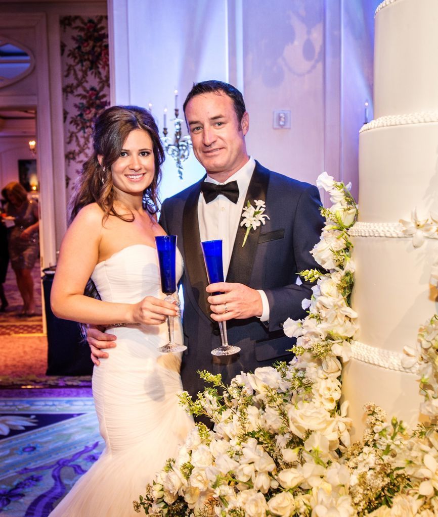 A bride and groom are posing for a picture in front of a wedding cake.