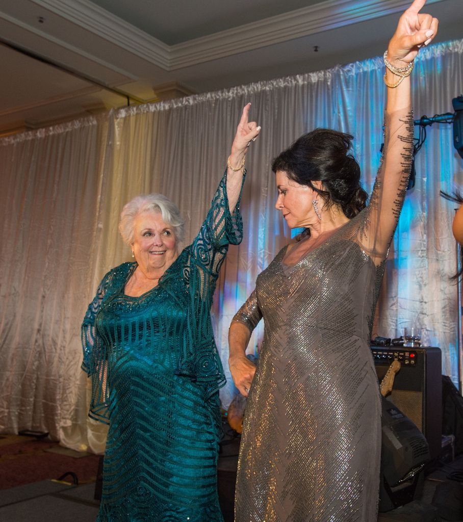 Two women are dancing on a stage with their arms in the air.