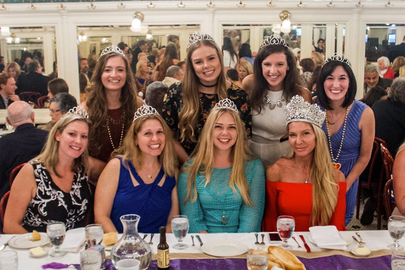 A group of women wearing tiaras are posing for a picture at a table.