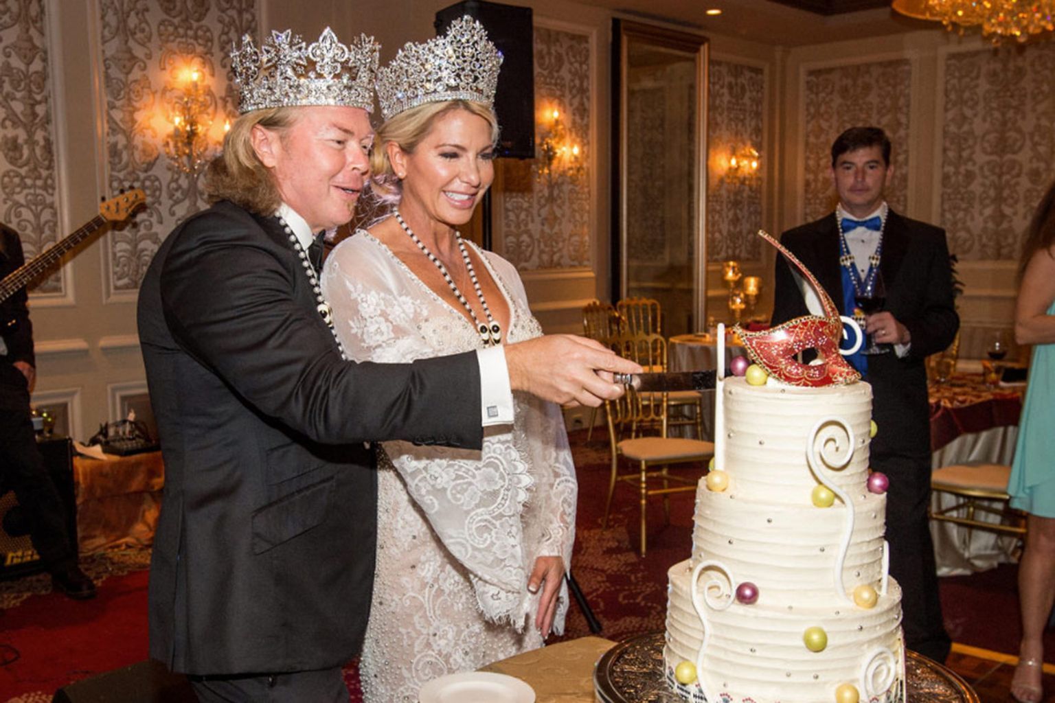 A bride and groom wearing crowns are cutting their wedding cake.