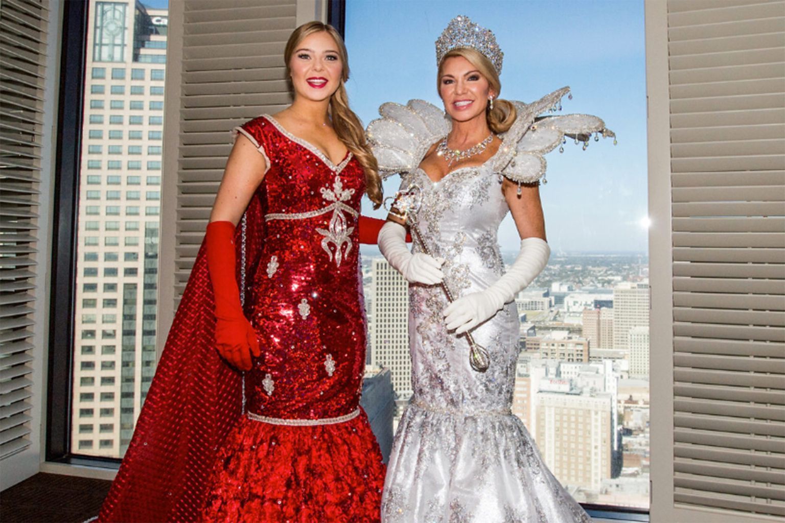 Two women in costume are standing next to each other in front of a window.