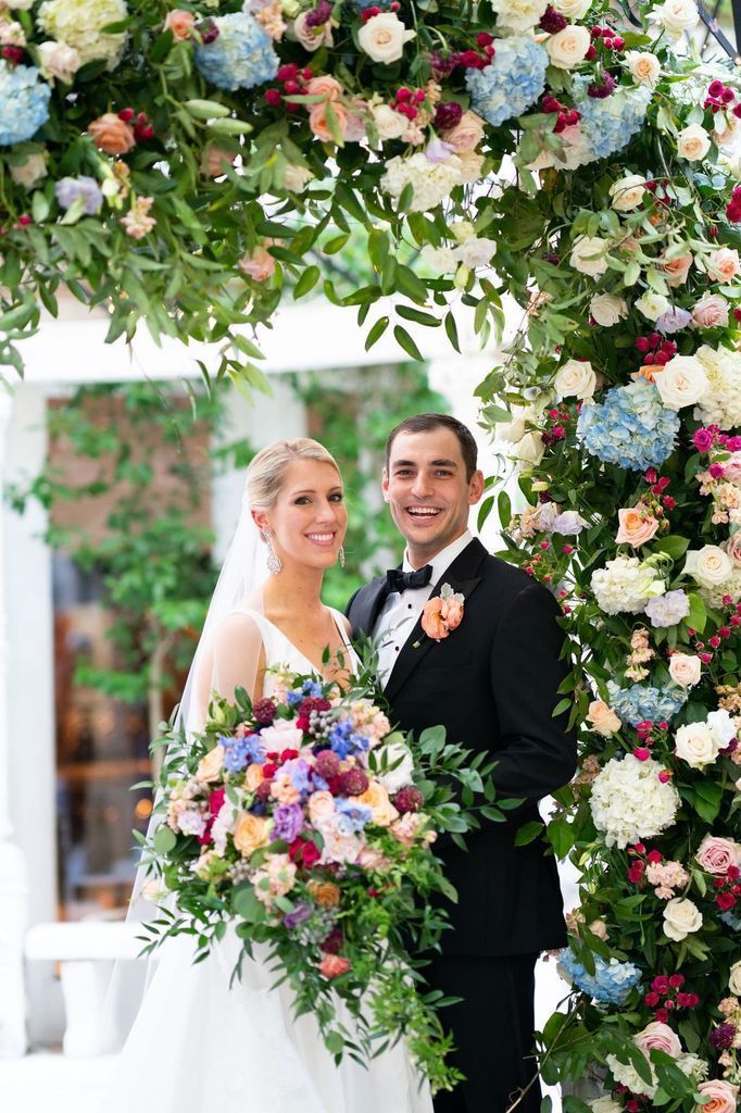 A bride and groom are posing for a picture under a floral arch.