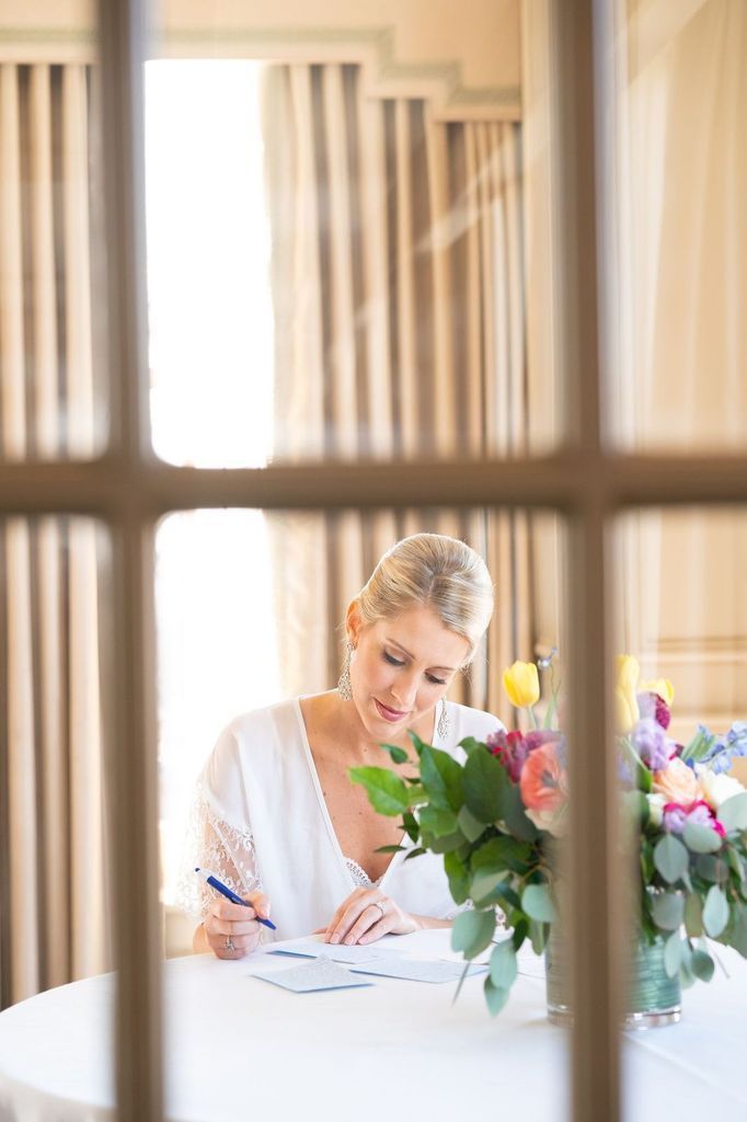 A woman is sitting at a table writing on a piece of paper.
