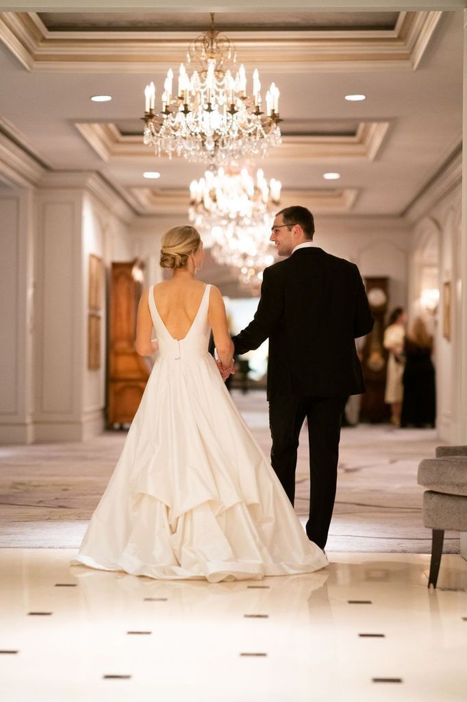 A bride and groom are walking down a hallway holding hands.