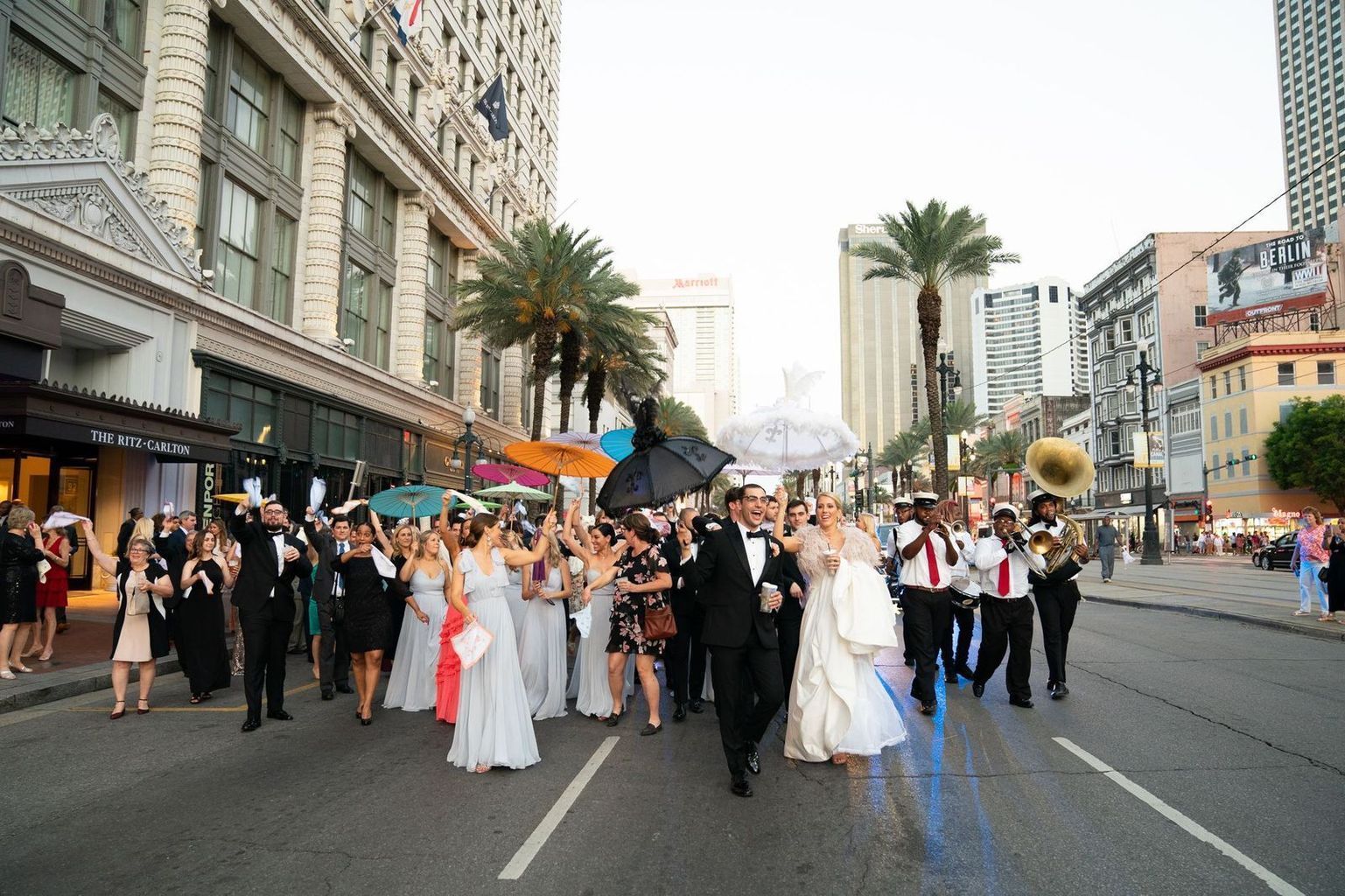 A bride and groom are walking down the street with a band behind them.
