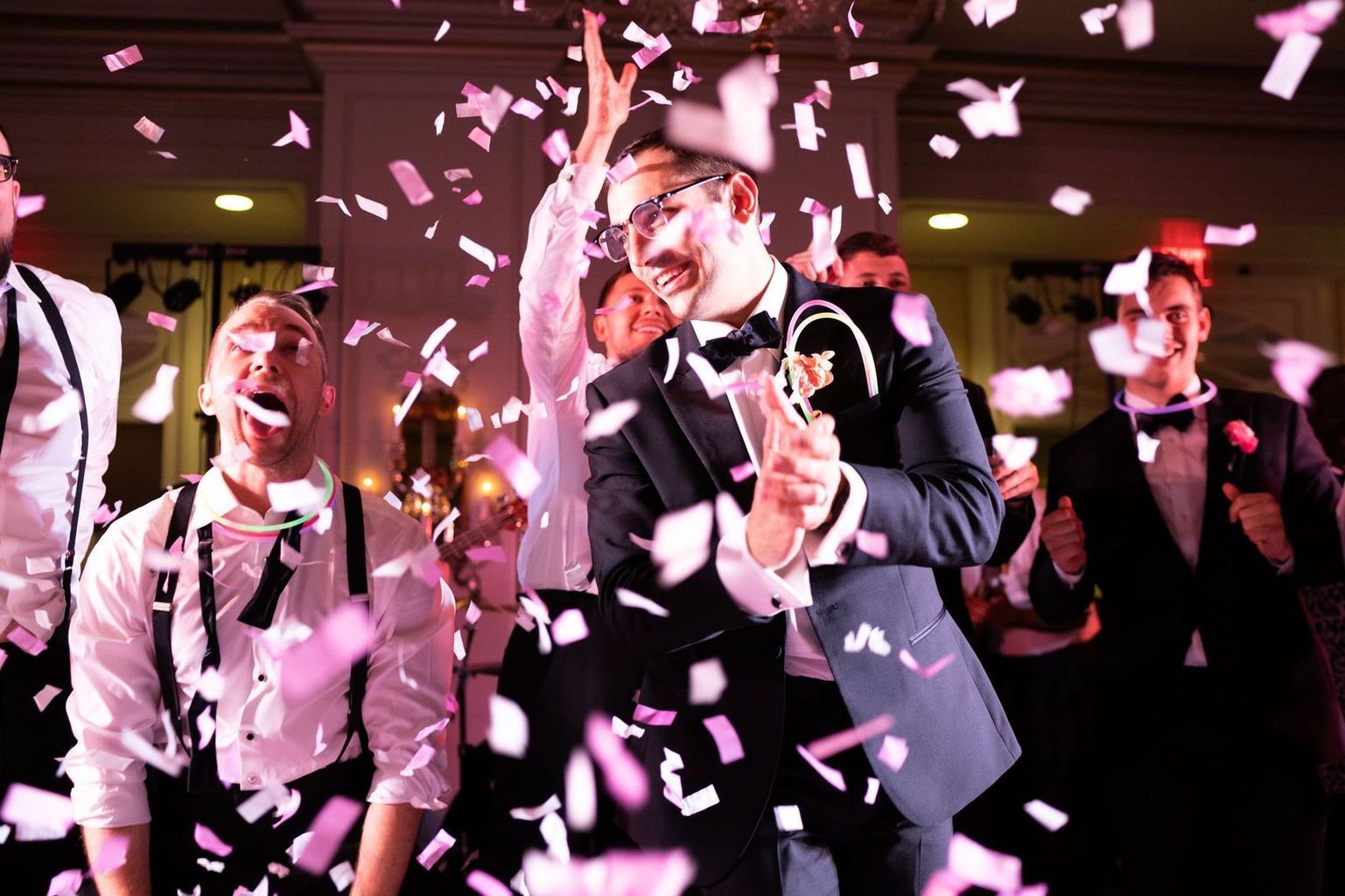 A man in a tuxedo is throwing confetti at a wedding reception.