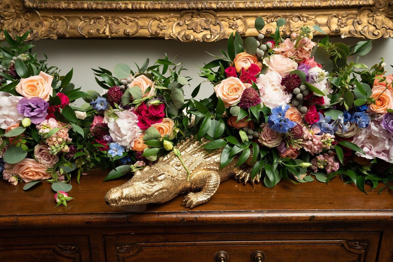 A statue of an alligator is sitting on a wooden table next to a bunch of flowers.