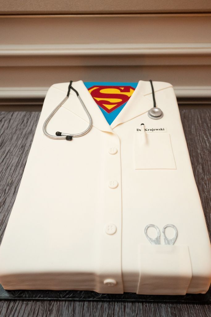 A cake that looks like a doctor 's coat with a superman logo on it.