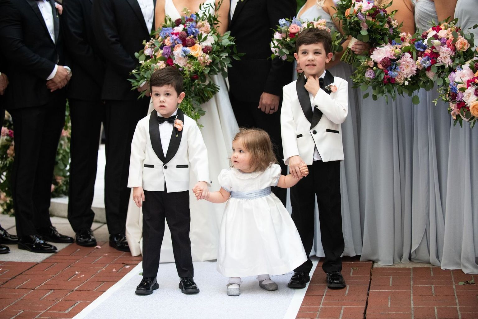 A flower girl and two ring bearers are walking down the aisle at a wedding.
