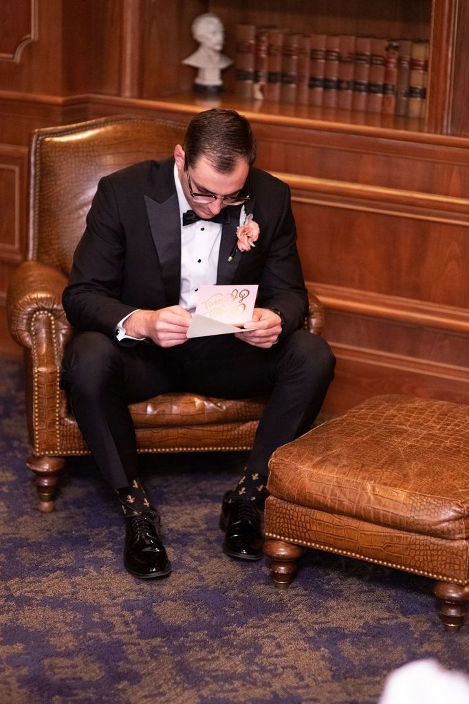 A man in a tuxedo is sitting in a chair reading a letter.