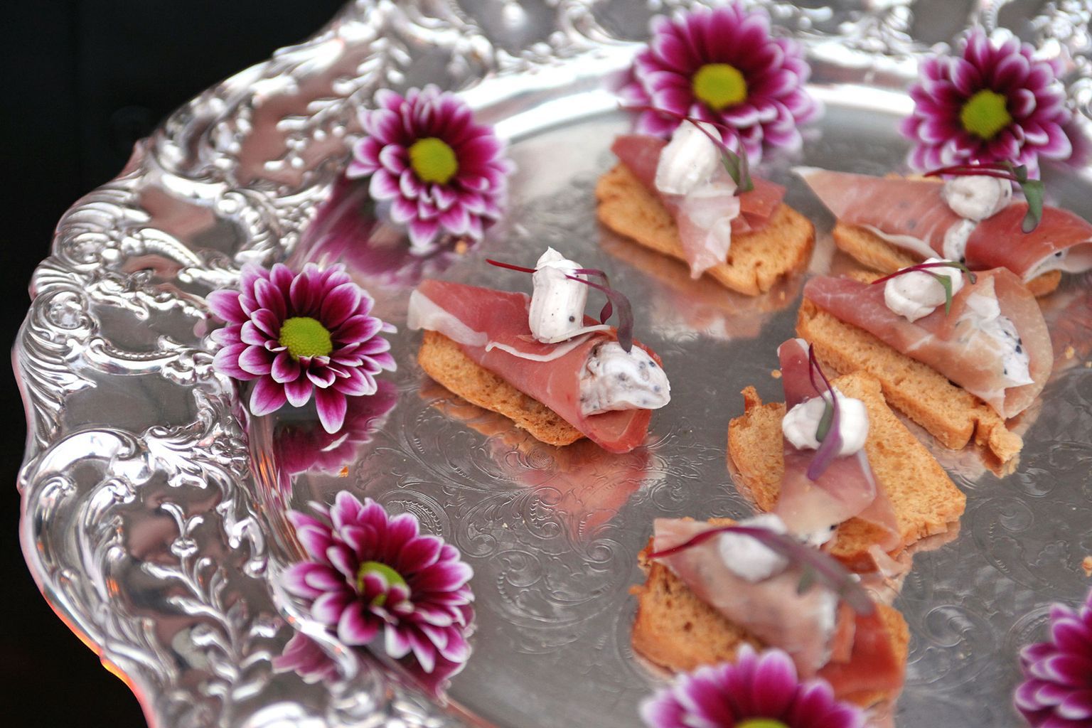 A silver plate topped with appetizers and purple flowers.