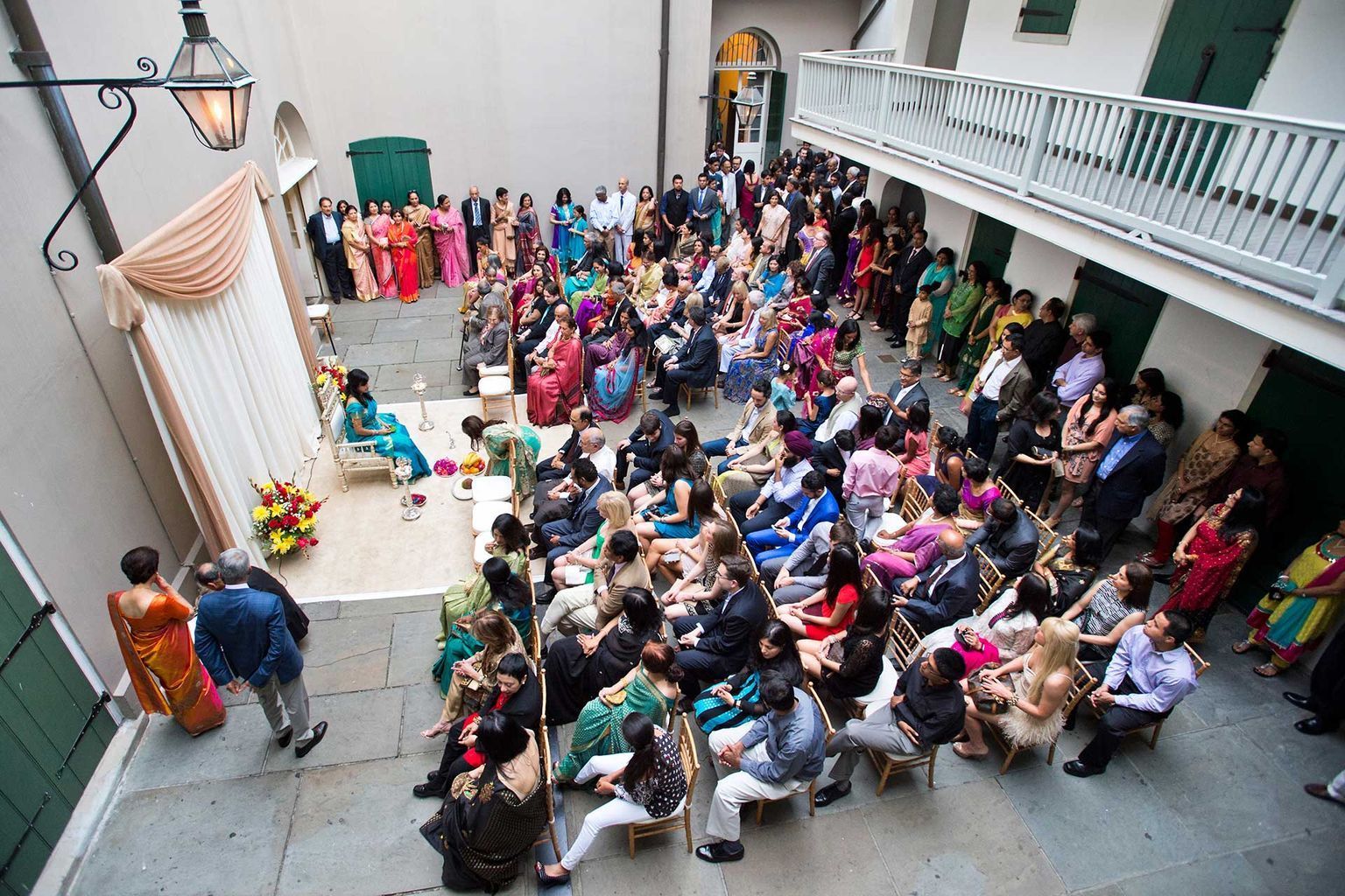 A large group of people are sitting in a courtyard watching a wedding ceremony.