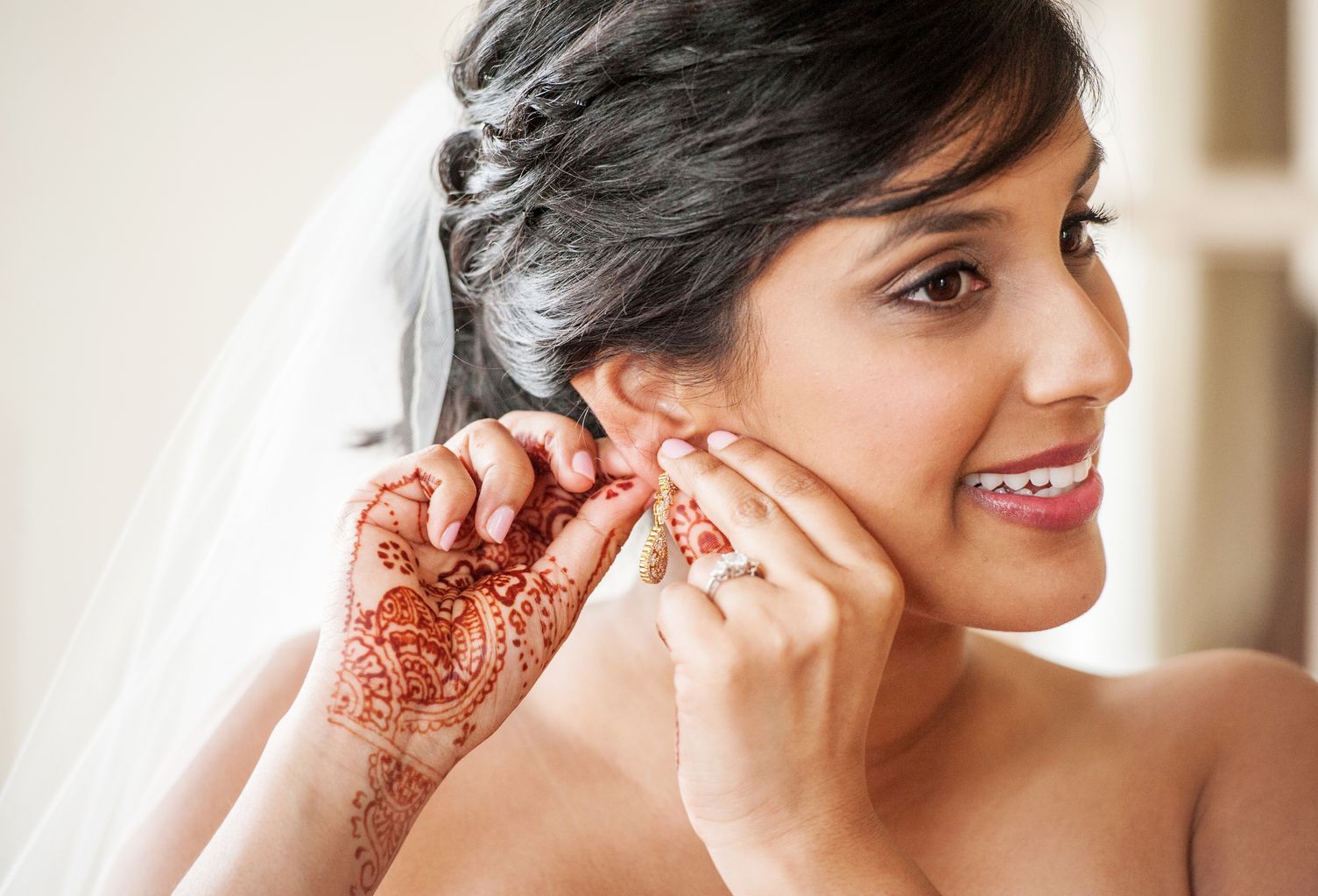 A woman with henna on her hand is putting on earrings.