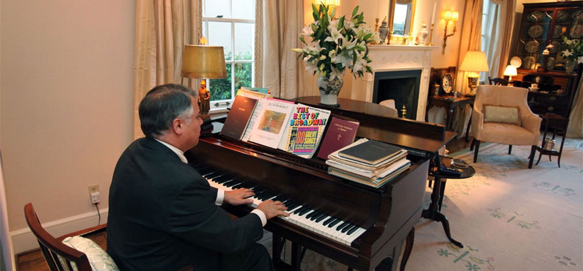 A man in a suit is playing a piano in a living room