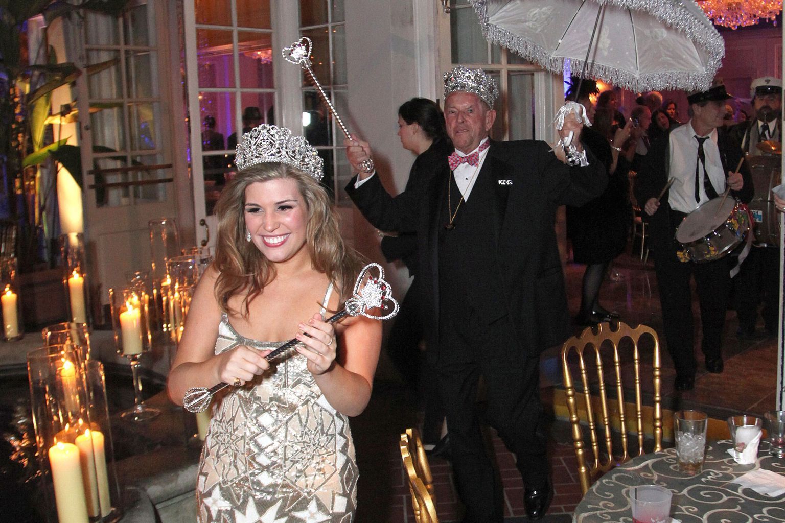 A woman is wearing a tiara and holding a wand while standing next to a man holding an umbrella.