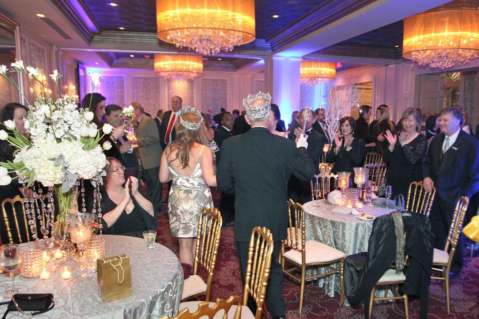 A group of people are dancing in a large room with tables and chairs.