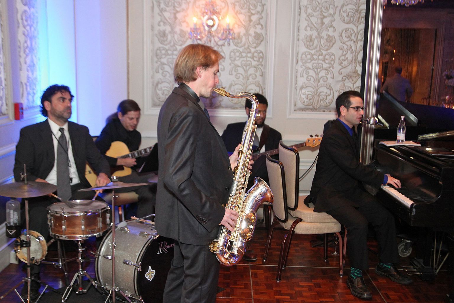 A man in a suit is playing a saxophone in a band.