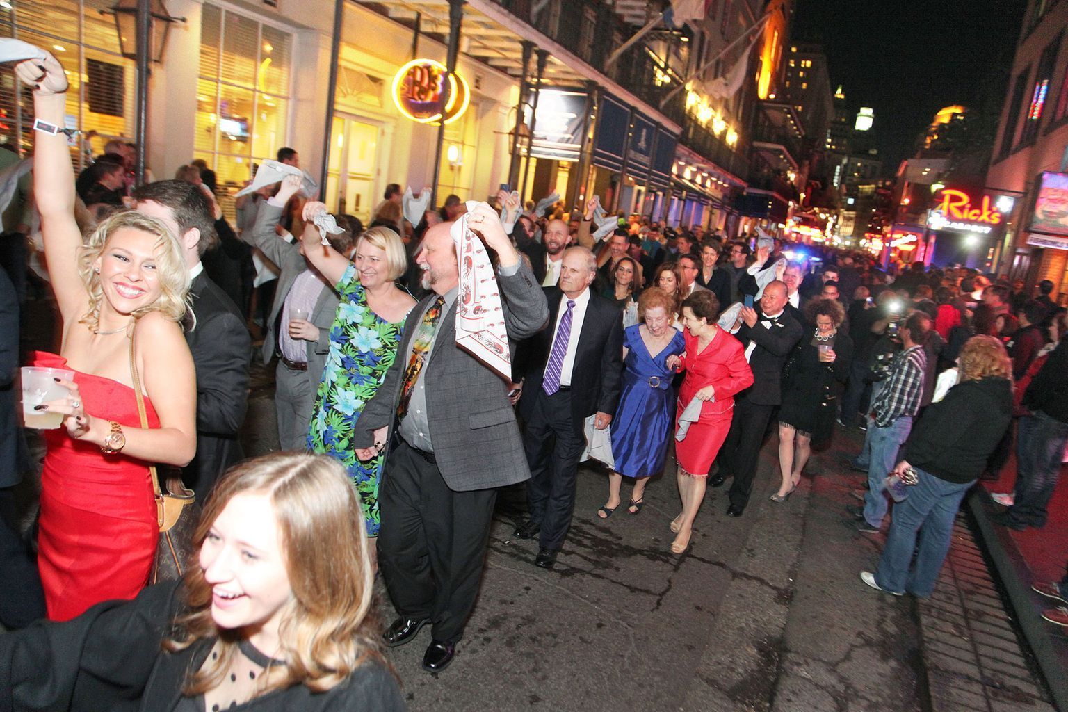 A crowd of people are walking down a street with a red sign in the background