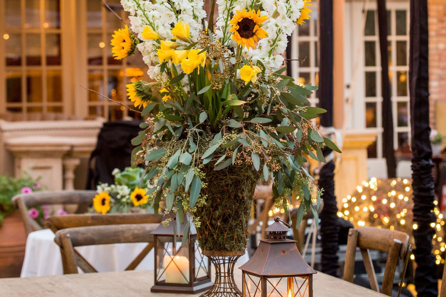 A table with a vase of flowers and lanterns on it.