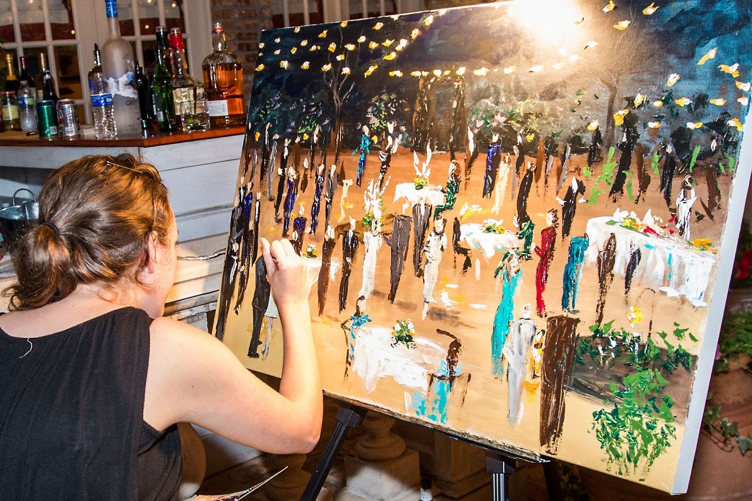 A woman is painting a picture of a wedding reception on an easel.