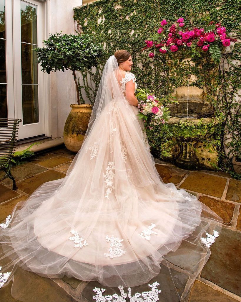 A bride in a wedding dress and veil is standing in front of a fountain.