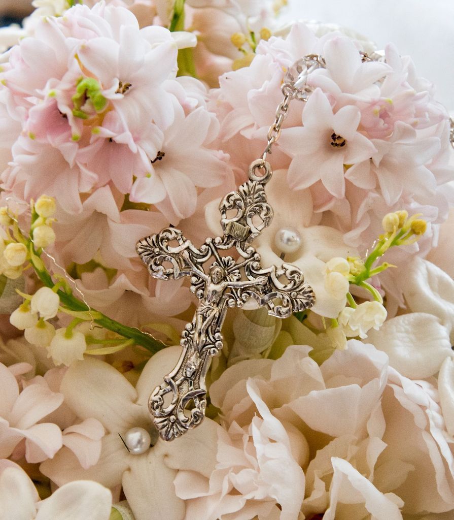 A silver cross is sitting on top of a bouquet of pink flowers