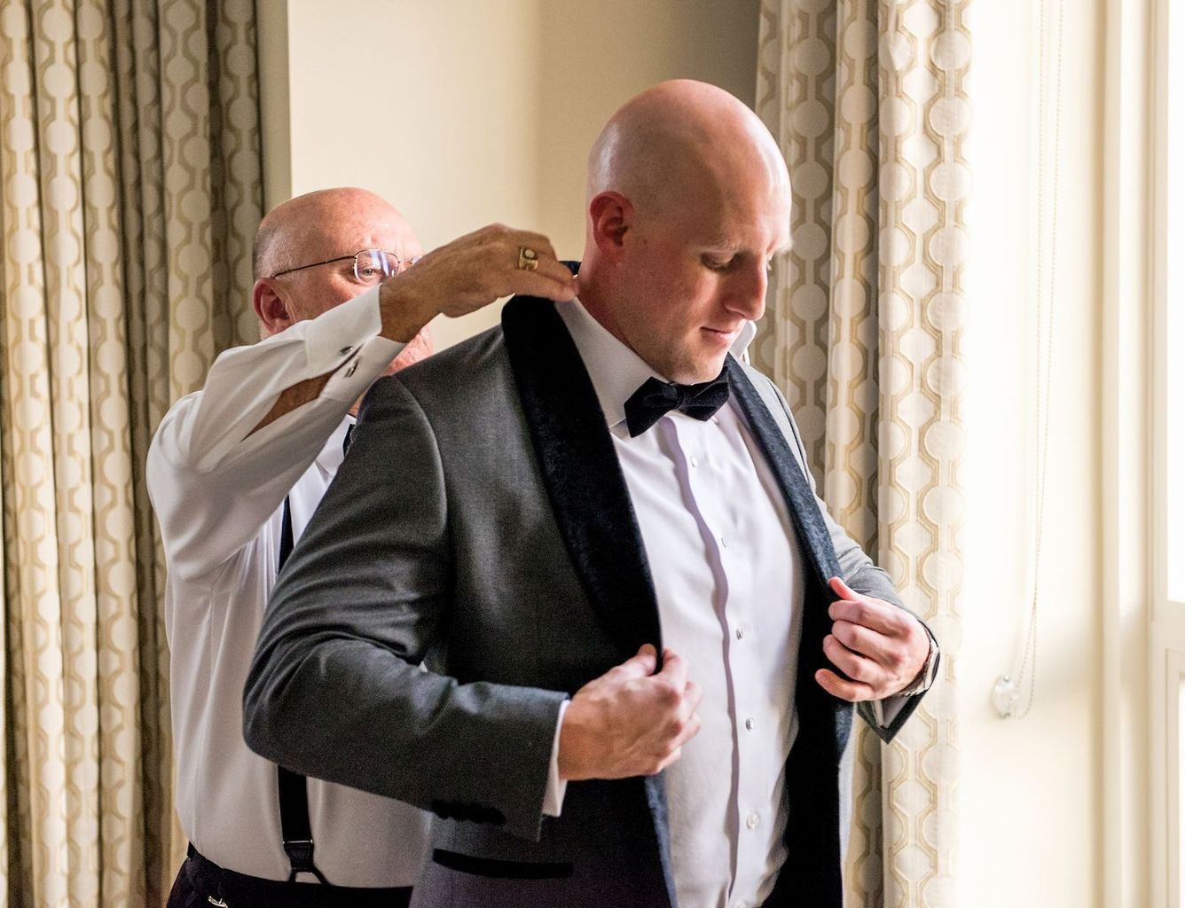 A man is helping another man put on a tuxedo.